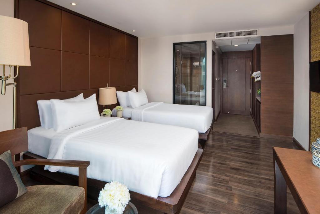 A bright twin room has two beds, a lounge chair, and a wood-floored entry area.