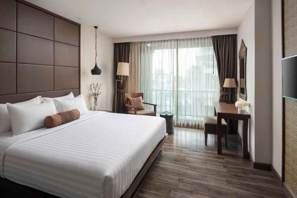 A bedroom with a large bed, lounge chair, desk and full-height curtained window.