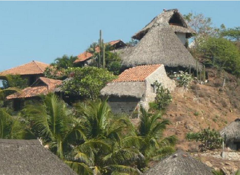 un groupe de maisons avec des toits de chaume et des palmiers dans l'établissement LA LOMA LINDA, Bungalows, Yoga and Feldenkrais, STARLINK INTERNET, à Zipolite