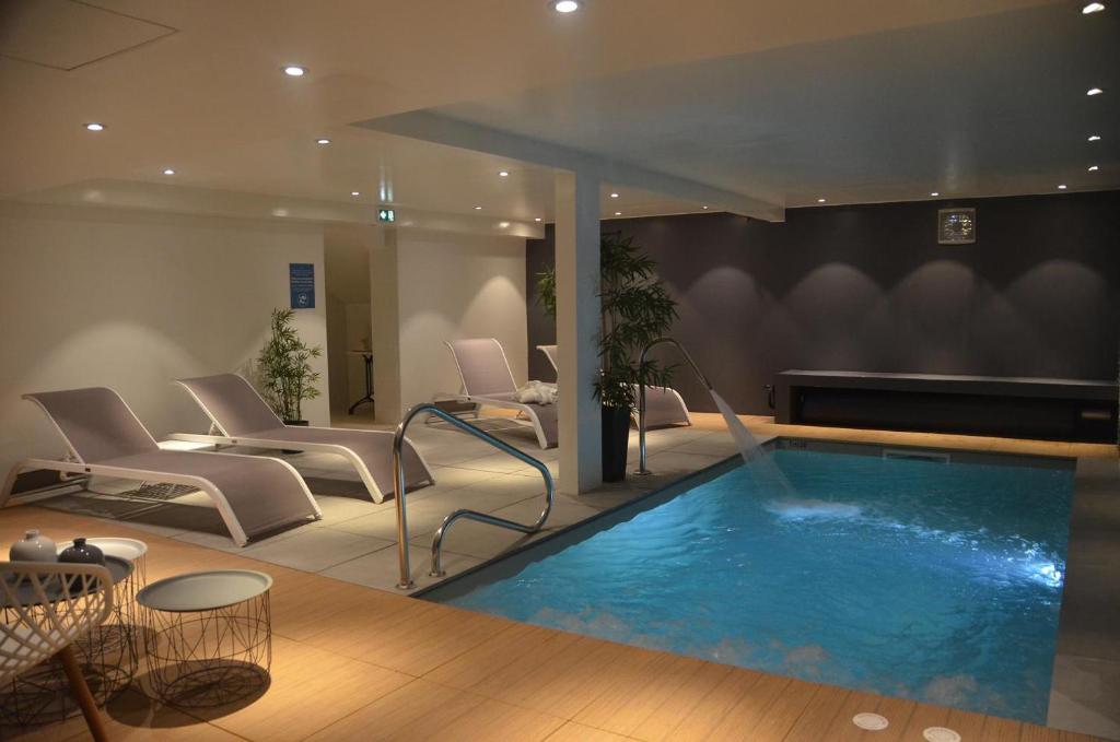 a pool in a room with chairs and a table at Hotel et Spa Les Cleunes Oléron in Saint-Trojan-les-Bains