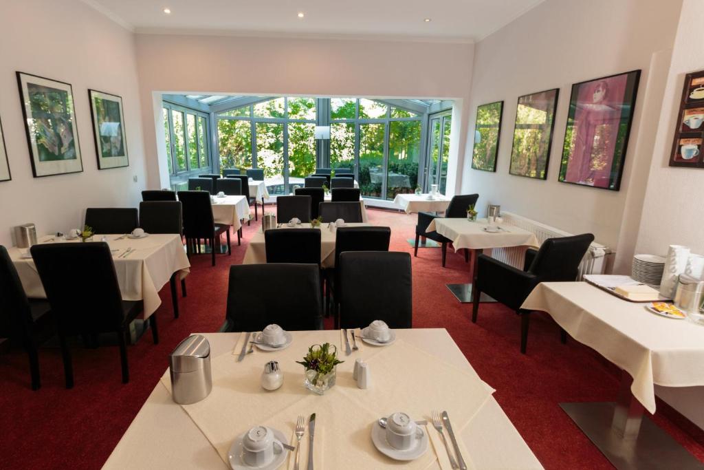 a restaurant with white tables and chairs and windows at Hotel Landhaus Schlachtensee in Berlin
