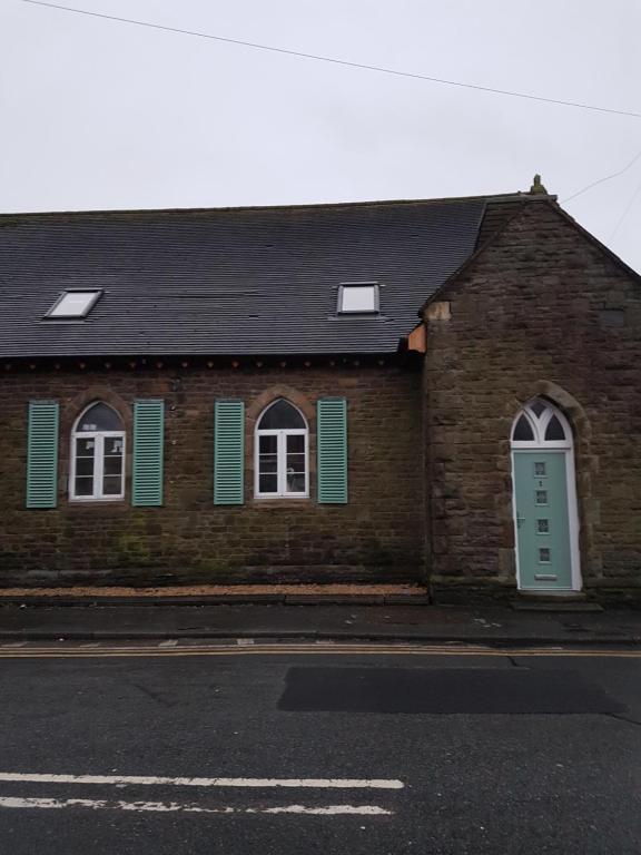 a brick building with green shutters and a blue door at Renovated Church close to the beach in Llanelli