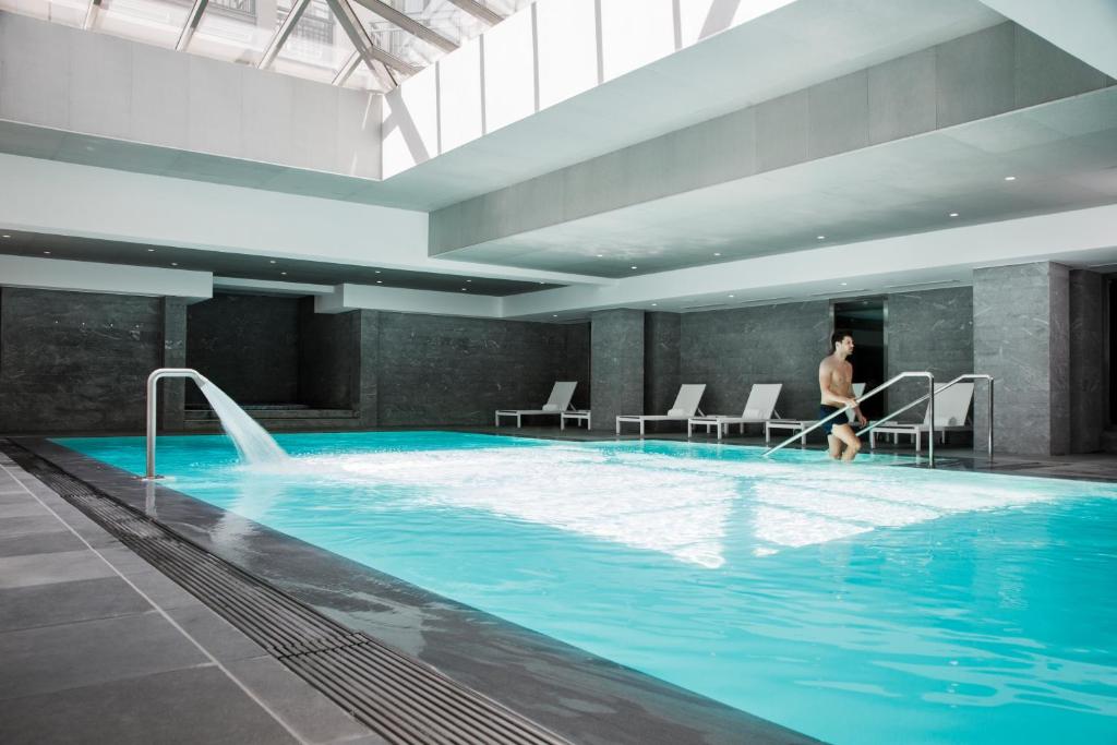 un hombre está caminando en una gran piscina en Relais Spa Chessy Val d'Europe en Chessy