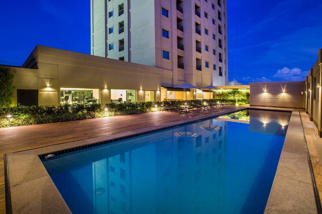 a swimming pool in front of a building at night at Hotel Araucaria Flat in Araraquara