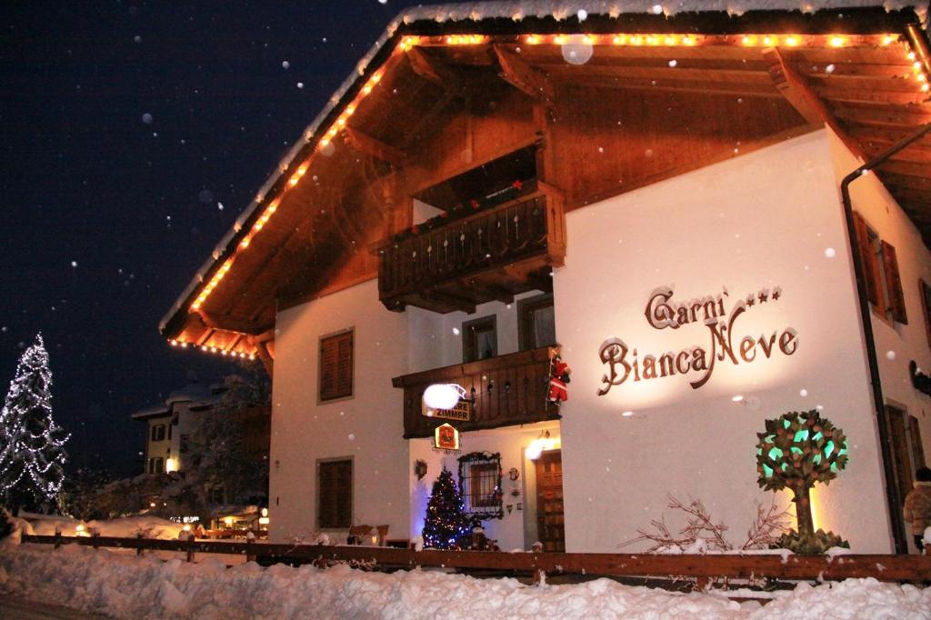 um edifício com luzes de Natal sobre ele na neve em Garni Biancaneve Ruffrè-Mendola em Mendola