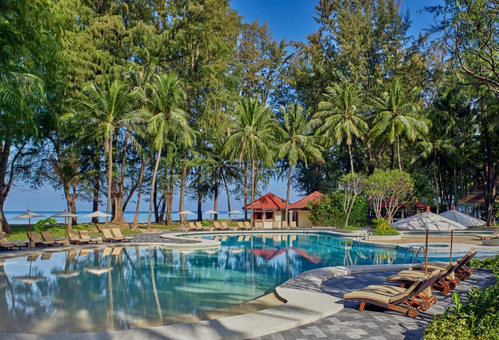 a swimming pool with lounge chairs and palm trees at Dusit Thani Laguna Phuket in Bang Tao Beach