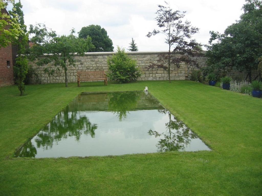 um lago no meio de um relvado com um banco em Le Clos Xavianne em Ribécourt-la-Tour