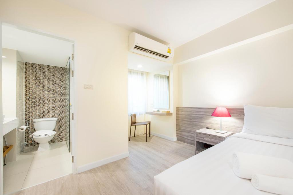 A bedroom photographed with its open bathroom entrance, work nook and air conditioner in view.
