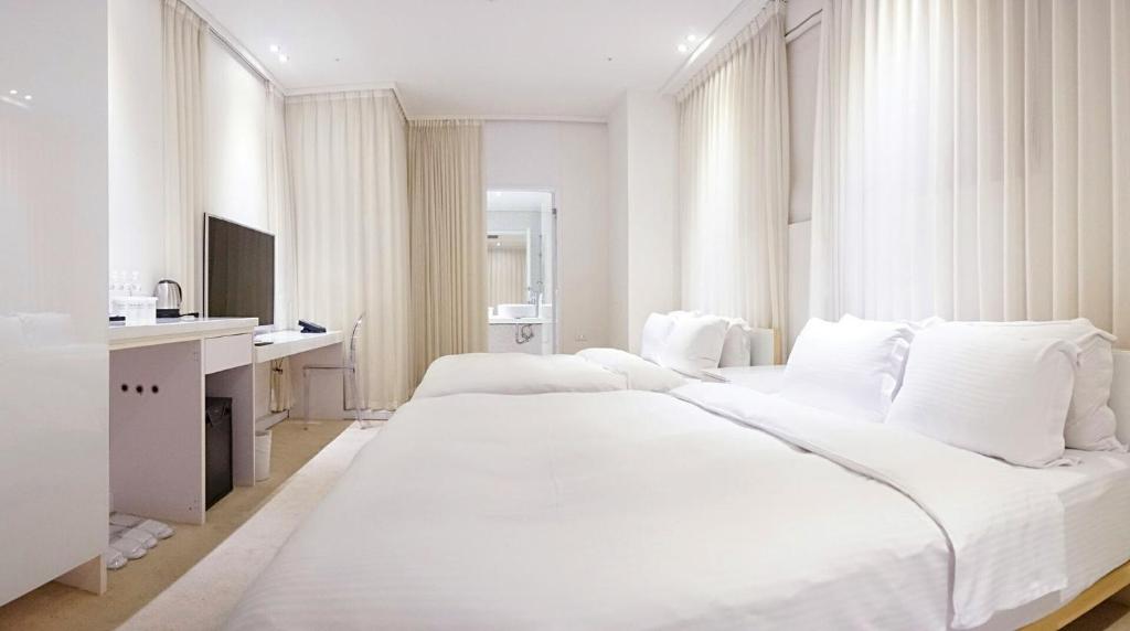 a white bedroom with two beds and a desk at The Tree House in Kaohsiung