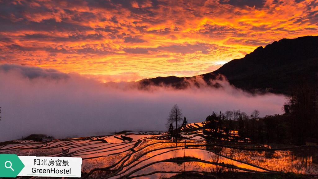 un tramonto tra le montagne con nuvole in primo piano di Green Hostel & Sunny Guesthouse a Yuanyang