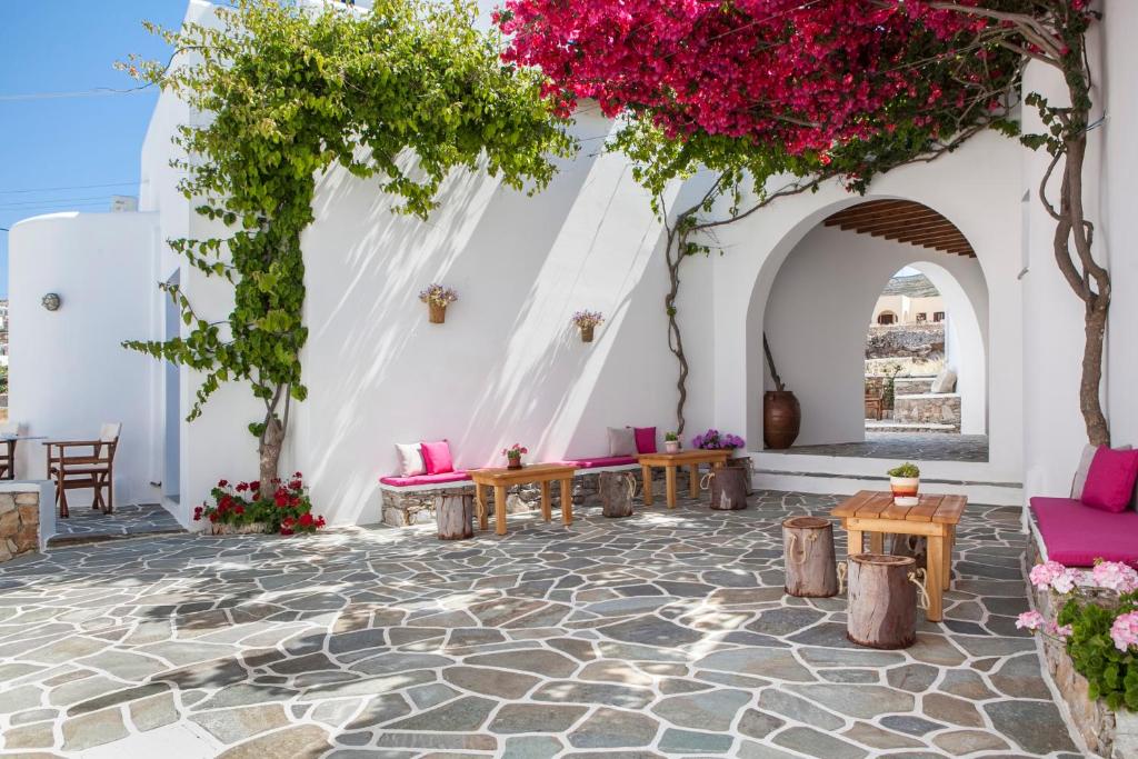un patio con muebles rosas y flores en una pared blanca en Aegeo Hotel, en Chora Folegandros