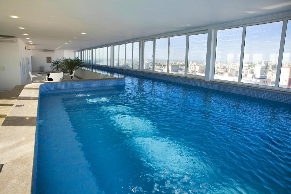 a large swimming pool in a building with windows at Plaza São Rafael Hotel - Próximo ao Cais Embarcadero e Hosp Santa Casa in Porto Alegre