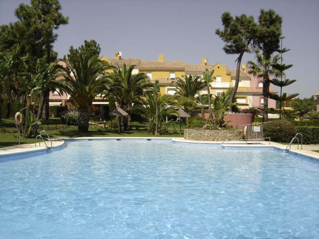 uma grande piscina num resort com palmeiras em Magnífico adosado de esquina con vistas al golf playas Islantilla em Islantilla