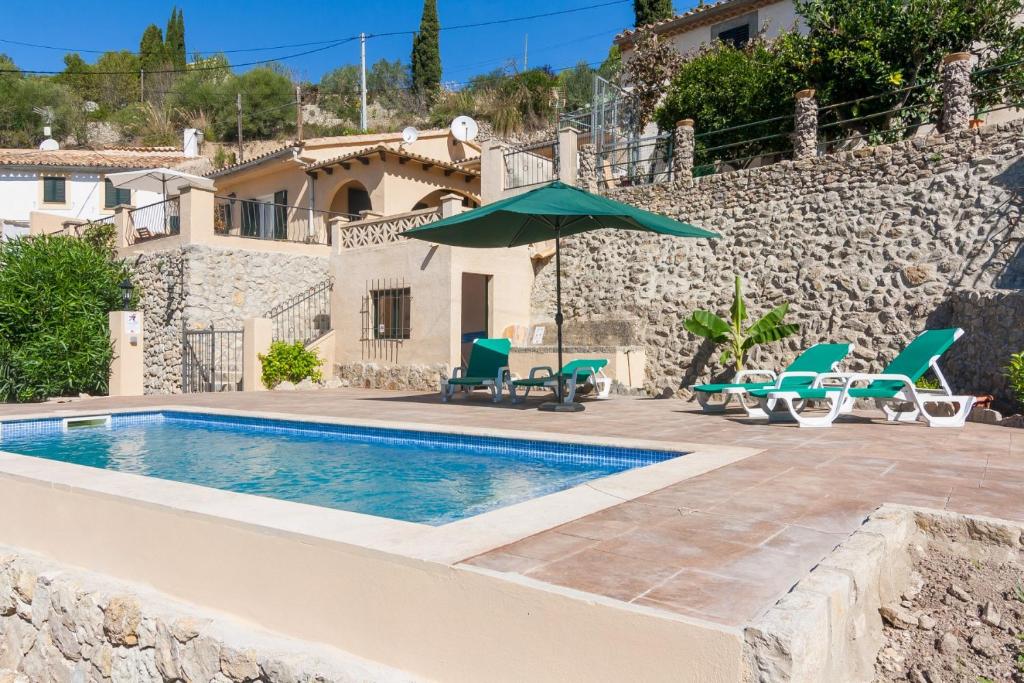 a pool with chairs and an umbrella next to a house at Sa Font in Puigpunyent