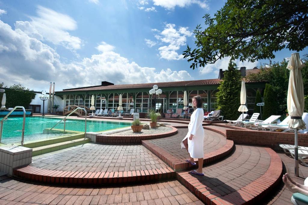 a woman is standing next to a swimming pool at Hotel Glockenspiel in Bad Griesbach