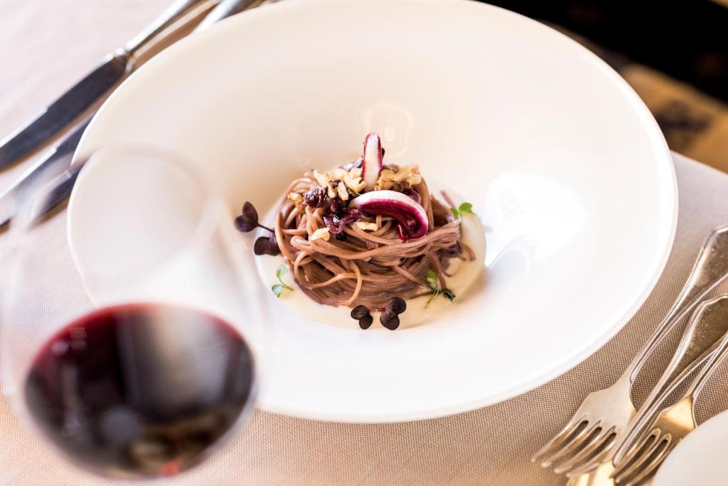 a white plate with pasta and a glass of wine at Hotel Genziana in Selva di Val Gardena