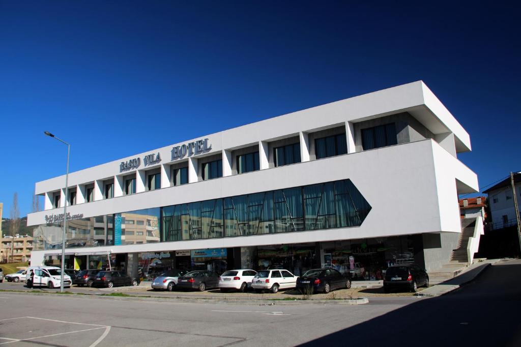 un gran edificio blanco con coches aparcados en un aparcamiento en Basto Vila Hotel en Cabeceiras de Basto