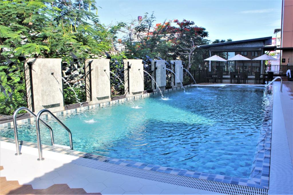 A long outdoor swimming pool bordered by greenery and a covered seating area.