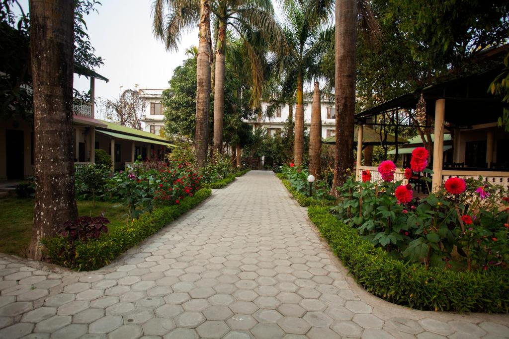 a pathway with flowers and palm trees and a building at Sauraha Resort in Sauraha