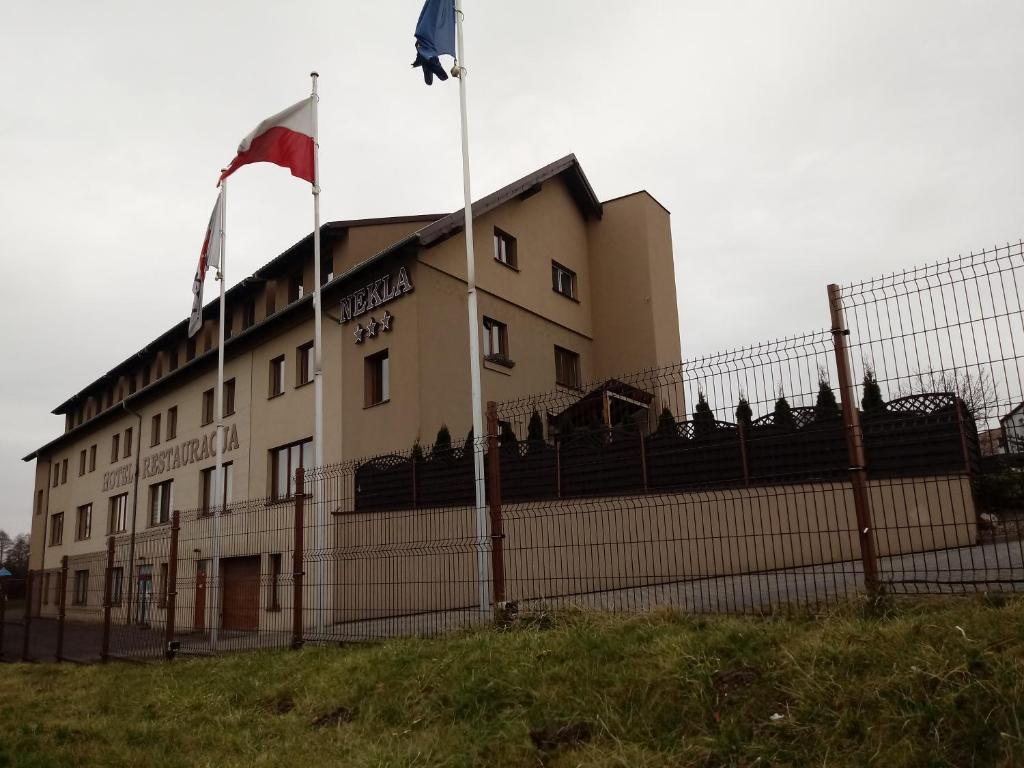a building with two flags in front of a fence at Hotel Nekla in Nekla