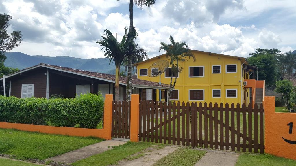 a yellow house with a fence and palm trees at Chalés Mar Virado in Ubatuba