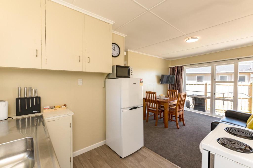 a kitchen and living room with a refrigerator and a table at Waitangi Beach Bach 30A in Paihia