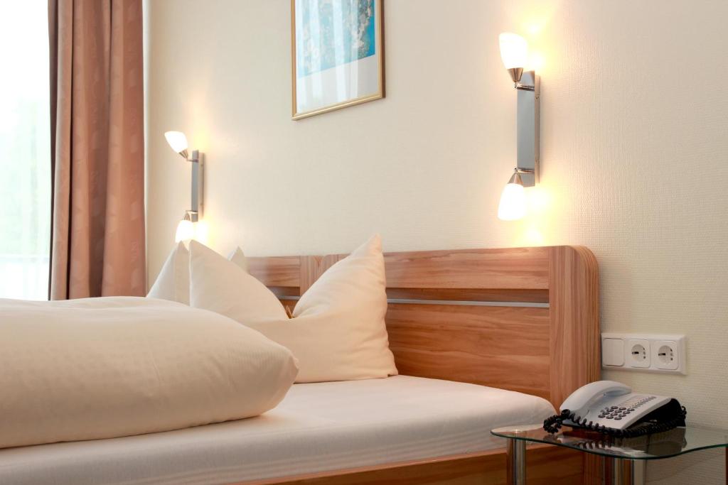 a bed with white pillows and a phone on a table at Hotel Schober am Kurpark in Bad Salzschlirf