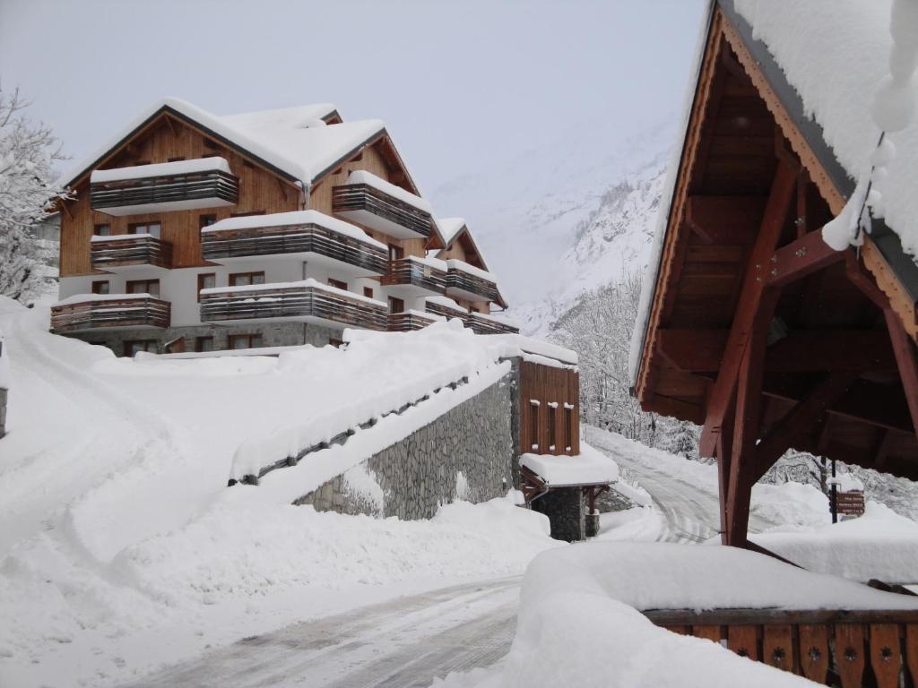 une maison recouverte de neige à côté d'une route dans l'établissement Résidence les Valmonts Vaujany, à Vaujany