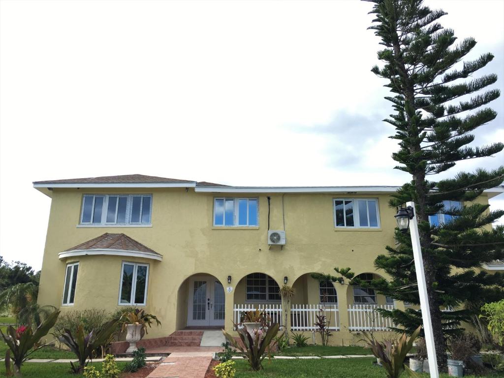 żółty dom z niebieskimi oknami i drzewem w obiekcie Golden Palms House w mieście Nassau