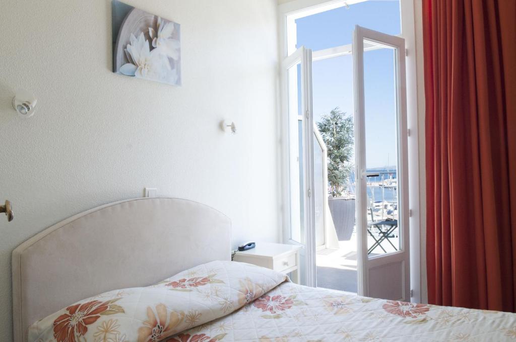 - une chambre avec un lit et une porte donnant sur un balcon dans l'établissement Hôtel Le Richiardi, à Carqueiranne