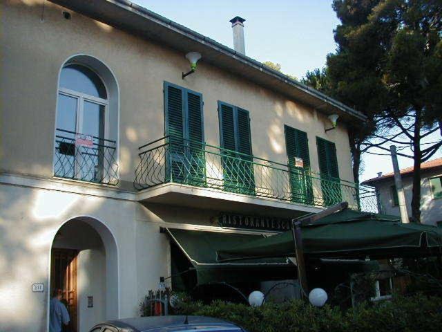 a white building with a balcony and a green umbrella at Rosignano Bed and Car in Castiglioncello