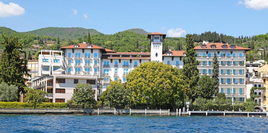 a building with a clock tower next to a body of water at Hotel Savoy Palace in Gardone Riviera