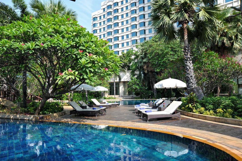 A landscaped outdoor pool bordered by loungers, umbrellas and dense tropical planting.