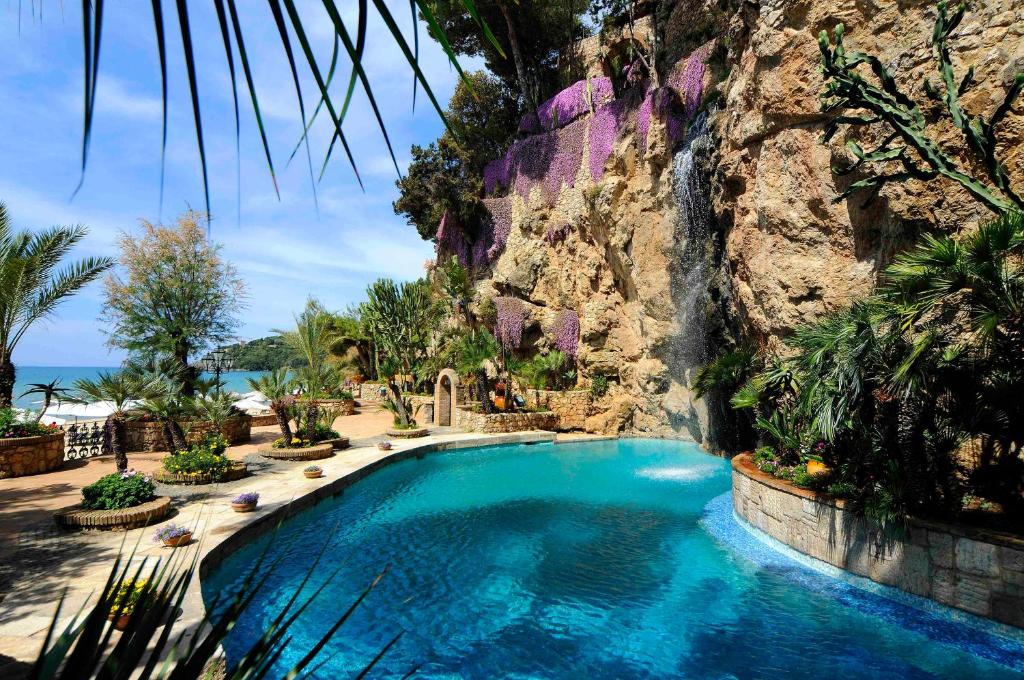 a swimming pool in front of a cliff with a waterfall at Aeneas' Landing Resort in Gaeta
