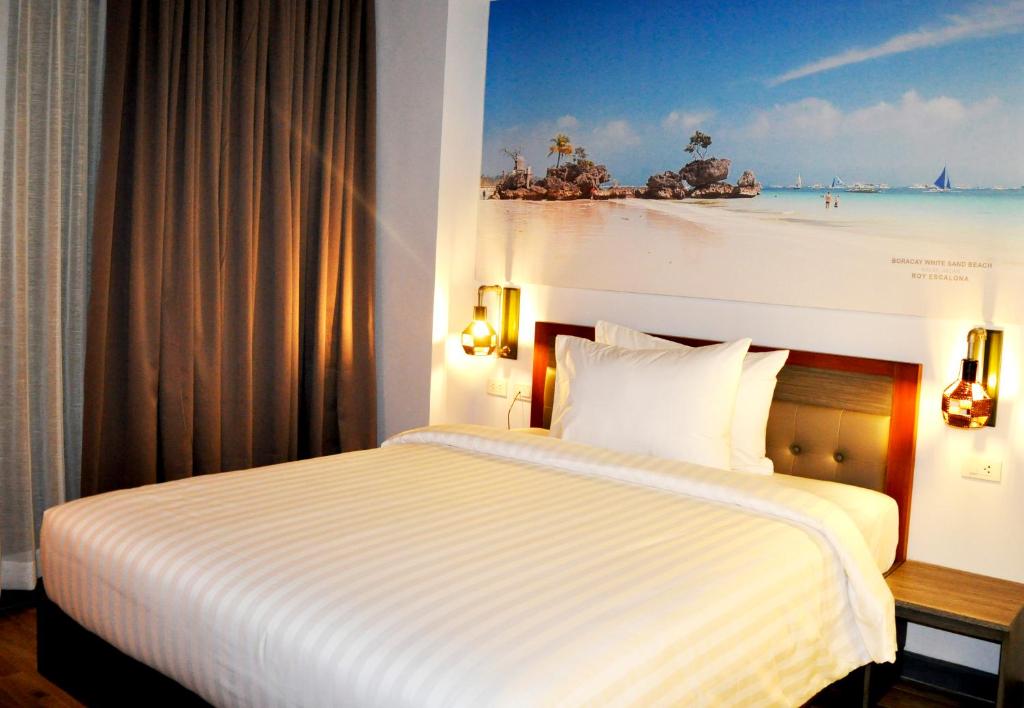 Cama en habitación de hotel con una pintura de playa en GQ Plaza en Kalibo