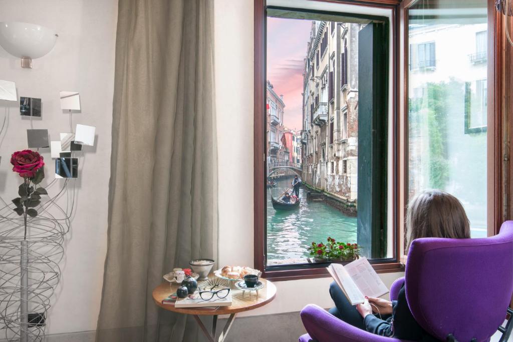 Eine Frau, die auf einem Stuhl sitzt und ein Buch am Fenster liest. in der Unterkunft Casa Flavia ai Morosini - Luxury apartment with Canal View in Venedig