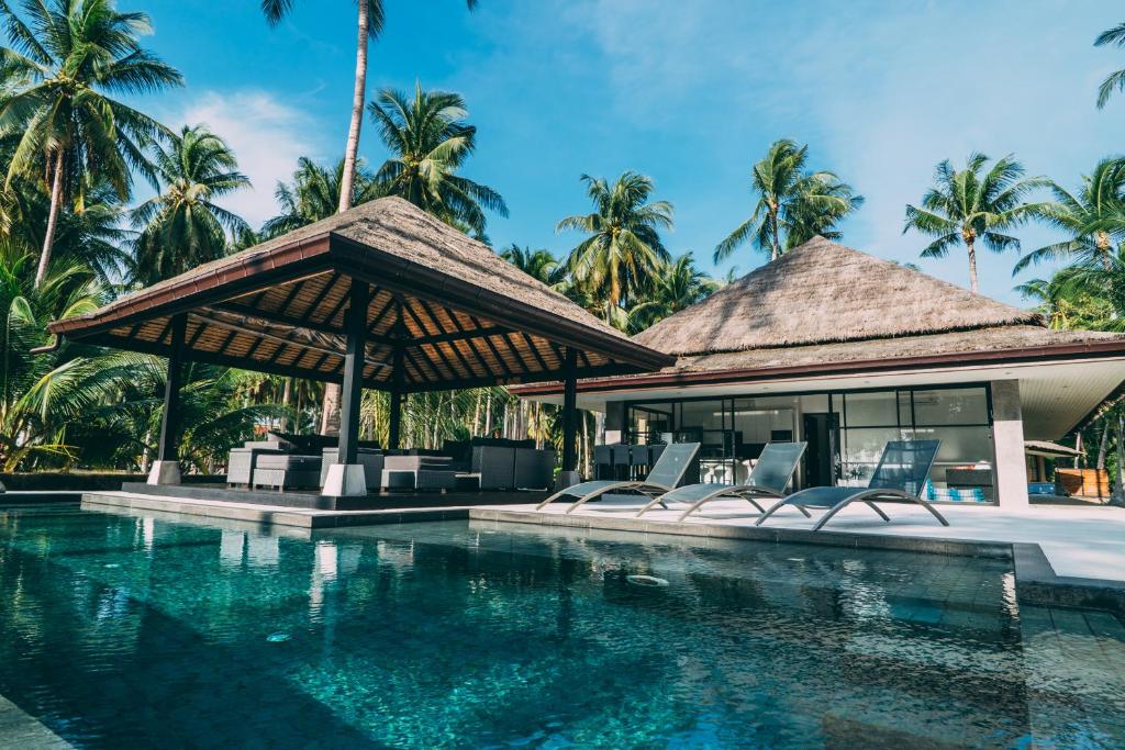 a resort with a swimming pool with chairs and palm trees at Le Motu in Taling Ngam Beach