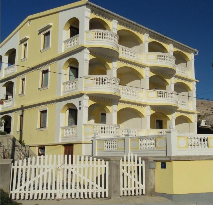 um edifício amarelo com uma cerca branca em frente em Villa Ana em Pag