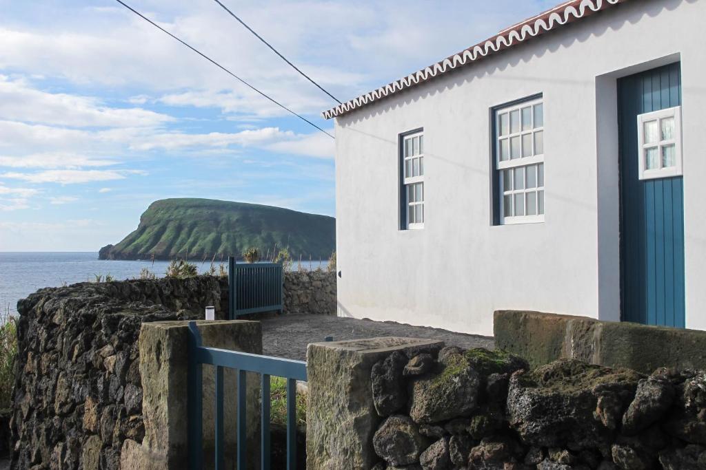 a white house with a stone wall next to the ocean at Canário do Mar - Rural Tourism in Angra do Heroísmo