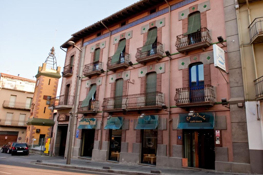 um edifício cor-de-rosa com varandas numa rua da cidade em Fonda Ca La Paula em Castellfollit de la Roca