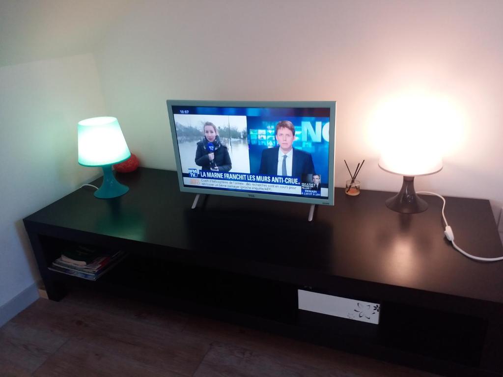 a flat screen tv sitting on a entertainment center with two lamps at Appartements T2 Proche de Rennes in Chantepie