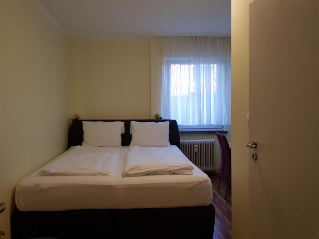 a bedroom with a bed with white sheets and a window at Hotel Dietrich in Neu Isenburg