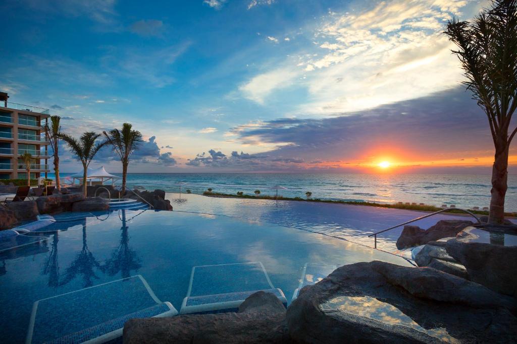 una piscina con vista al mar al atardecer en Hard Rock Hotel Cancun - All Inclusive, en Cancún