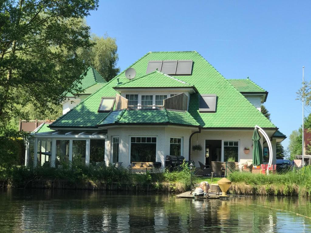 a house with a green roof on the water at Moderne Maisonette-Wohnung am Karpfenteich; modern Apartment with view of the carp pond in Barmstedt