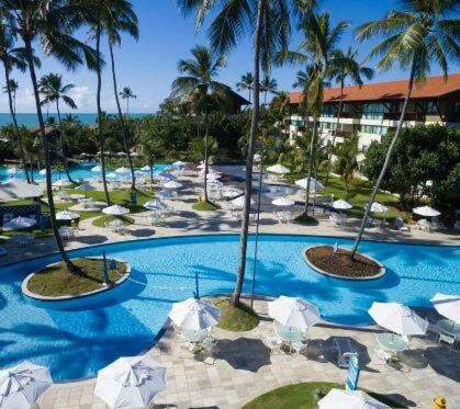 a resort with a pool with palm trees and umbrellas at Marulhos suítes e resorts in Porto De Galinhas