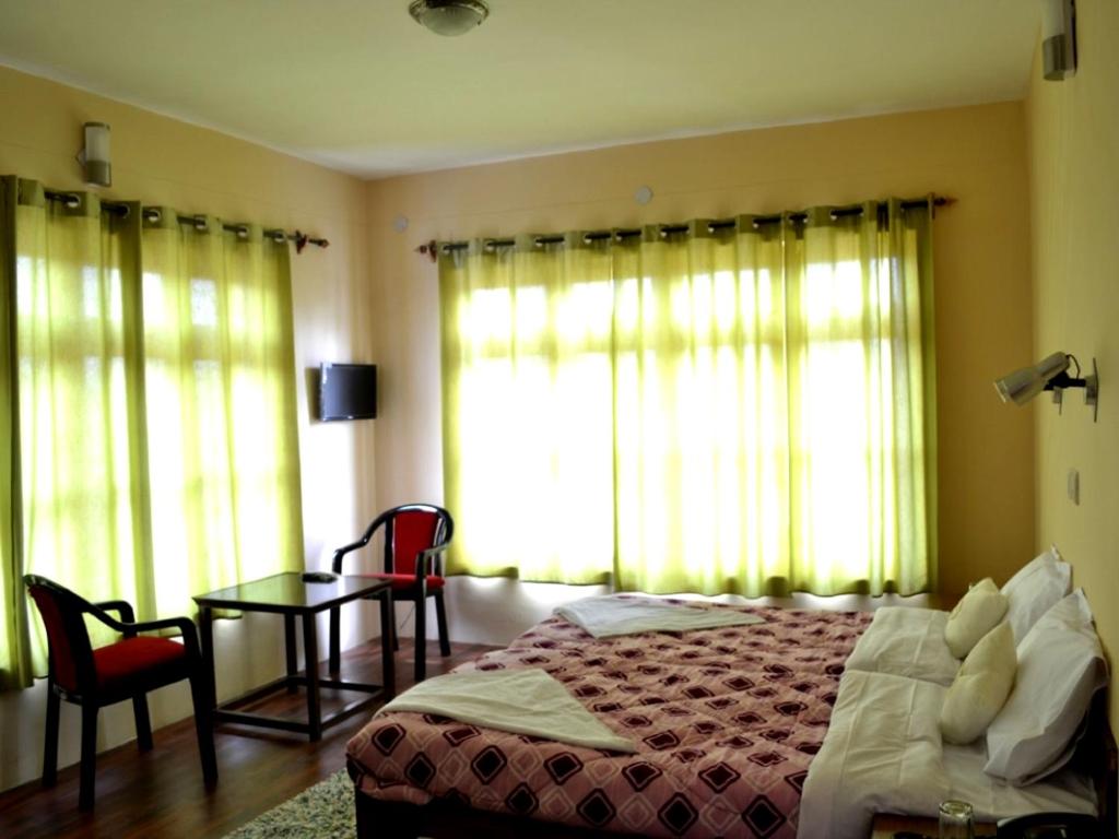 a bedroom with a bed and a table and windows at Hotel Ladakh Heaven in Leh