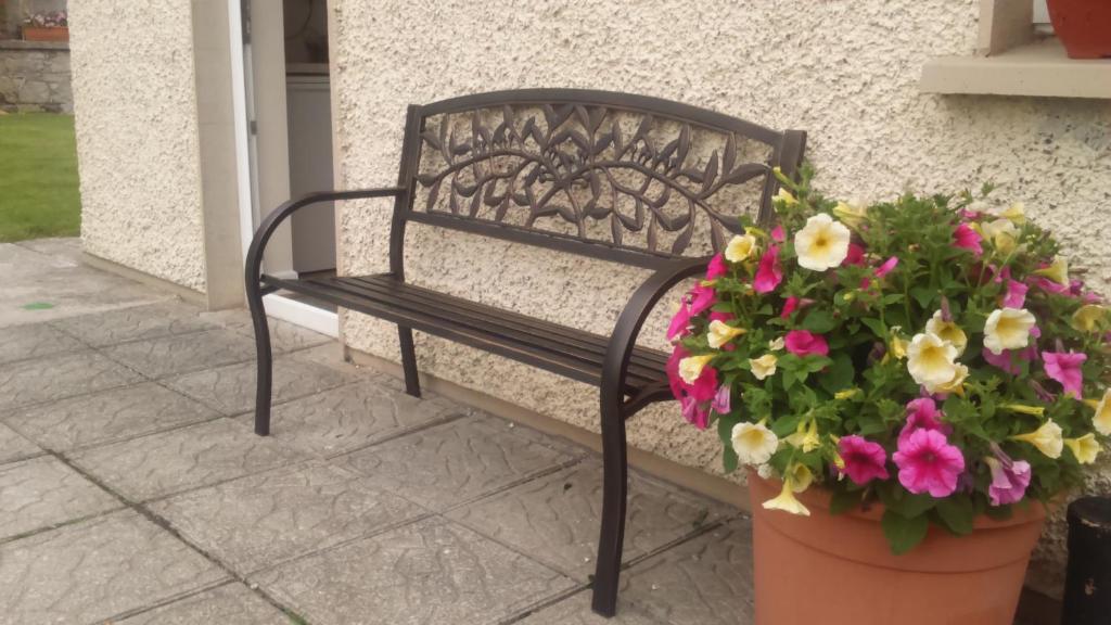 a black bench sitting next to a wall with flowers at Nick & Sandra's in Slane