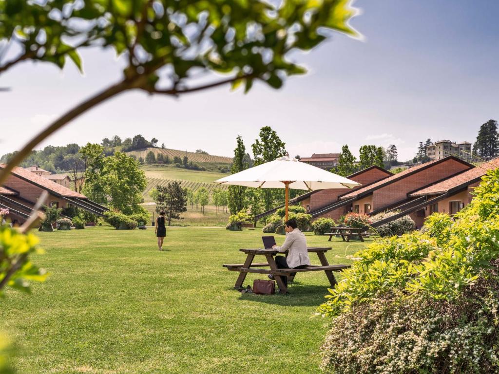 a woman sitting at a picnic table under an umbrella at Serravalle Golf Hotel in Serravalle Scrivia