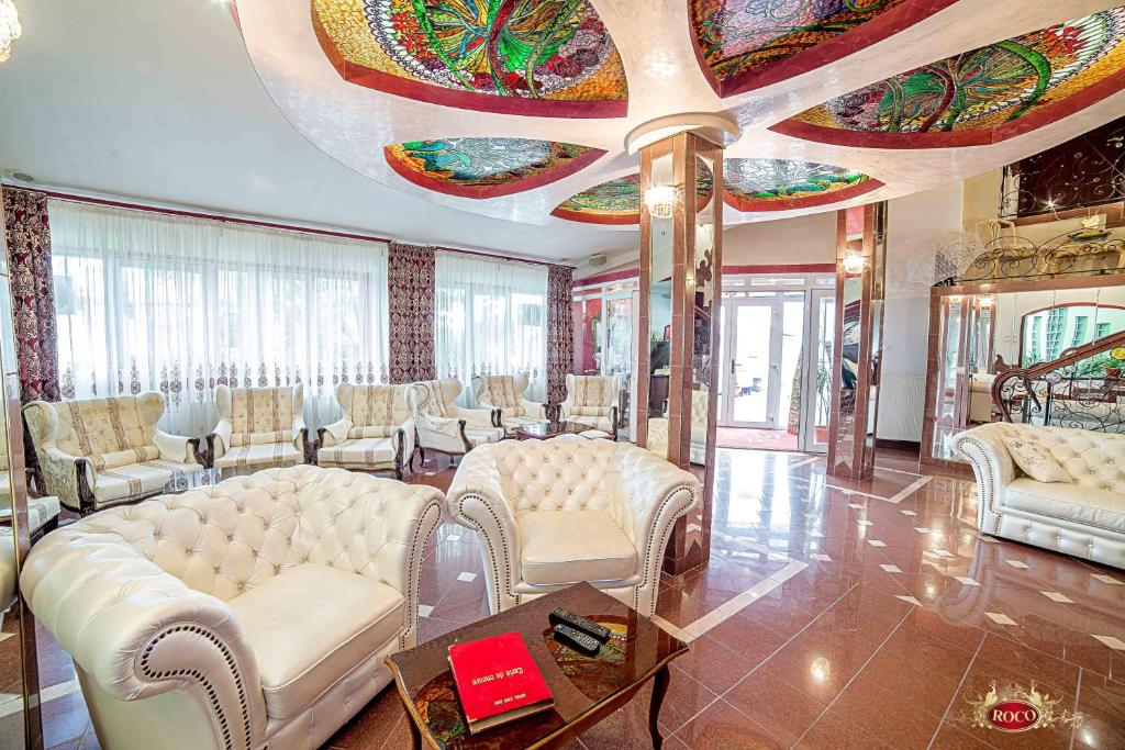 a living room with white furniture and a ceiling with a painting at Hotel Roco in Izvin