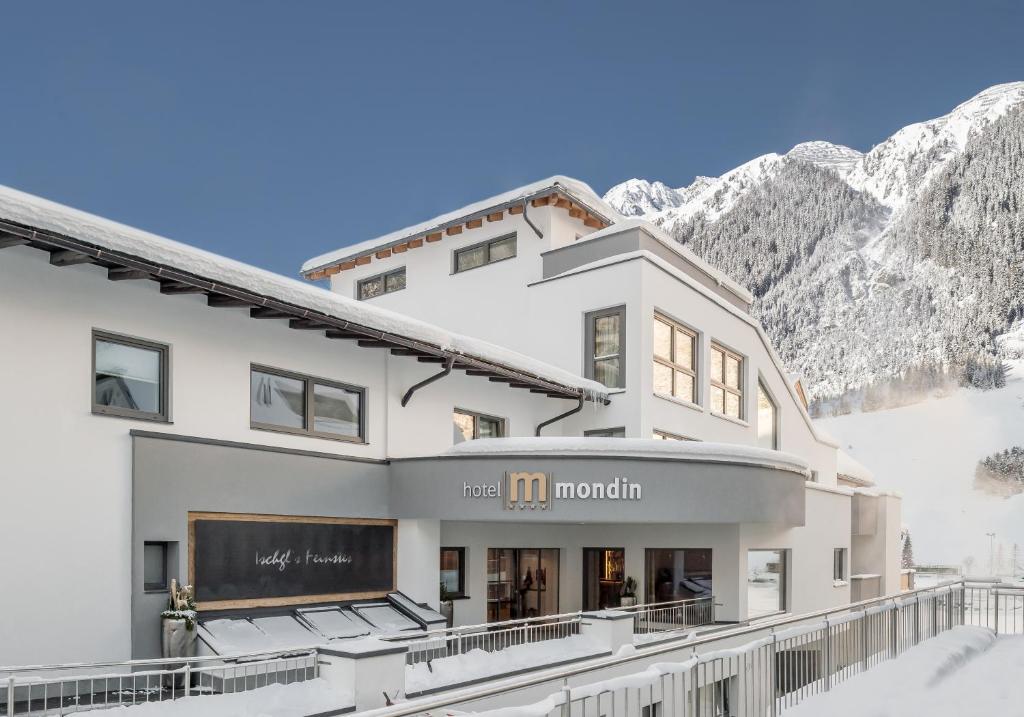 um grande edifício branco com montanhas ao fundo em Hotel Mondin em Ischgl